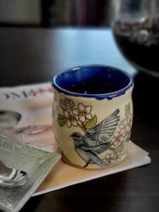 A handmade ceramic mug with bluebirds inlayed into the clay and handpainted.