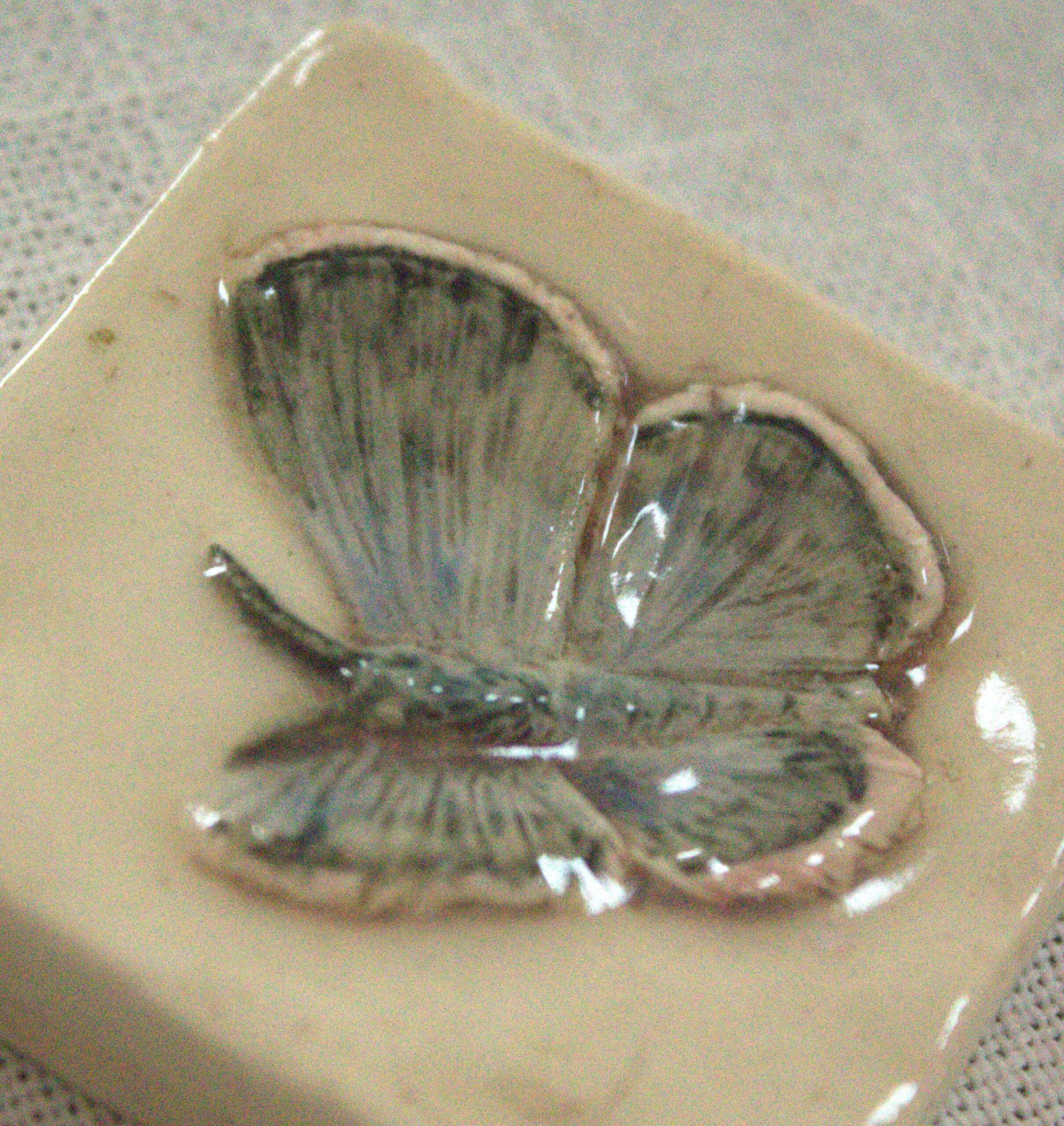 Closeup photo of the carving details in the silvery blue 2 inch butterfly tile crafted by Fire Creek Clay